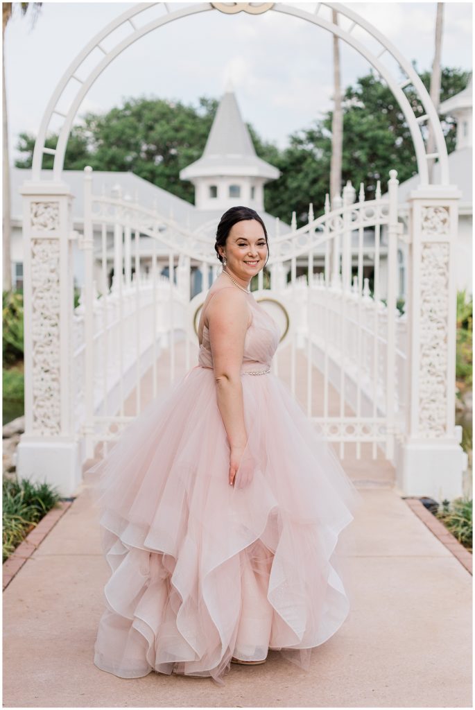 Disney bride at pink gown out front of gate smiling