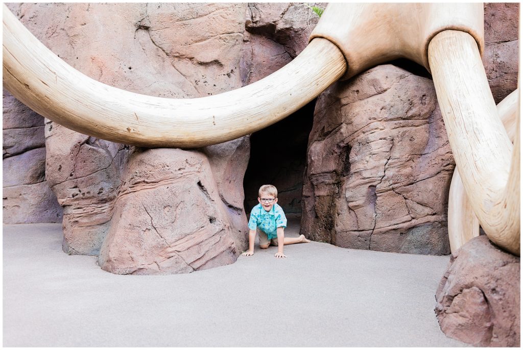 boy crawling on the ground around elephant skull bones at Art of Animation in the Lion King section