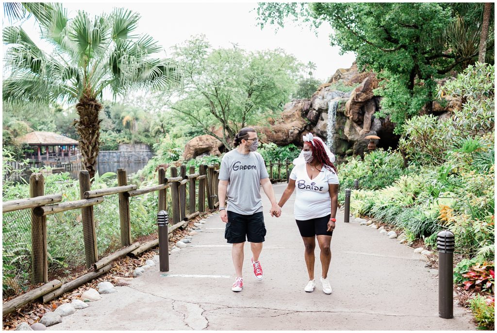 engaged couple holding hands and walking towards camera looking at each other in Disney's Animal Kingdom
